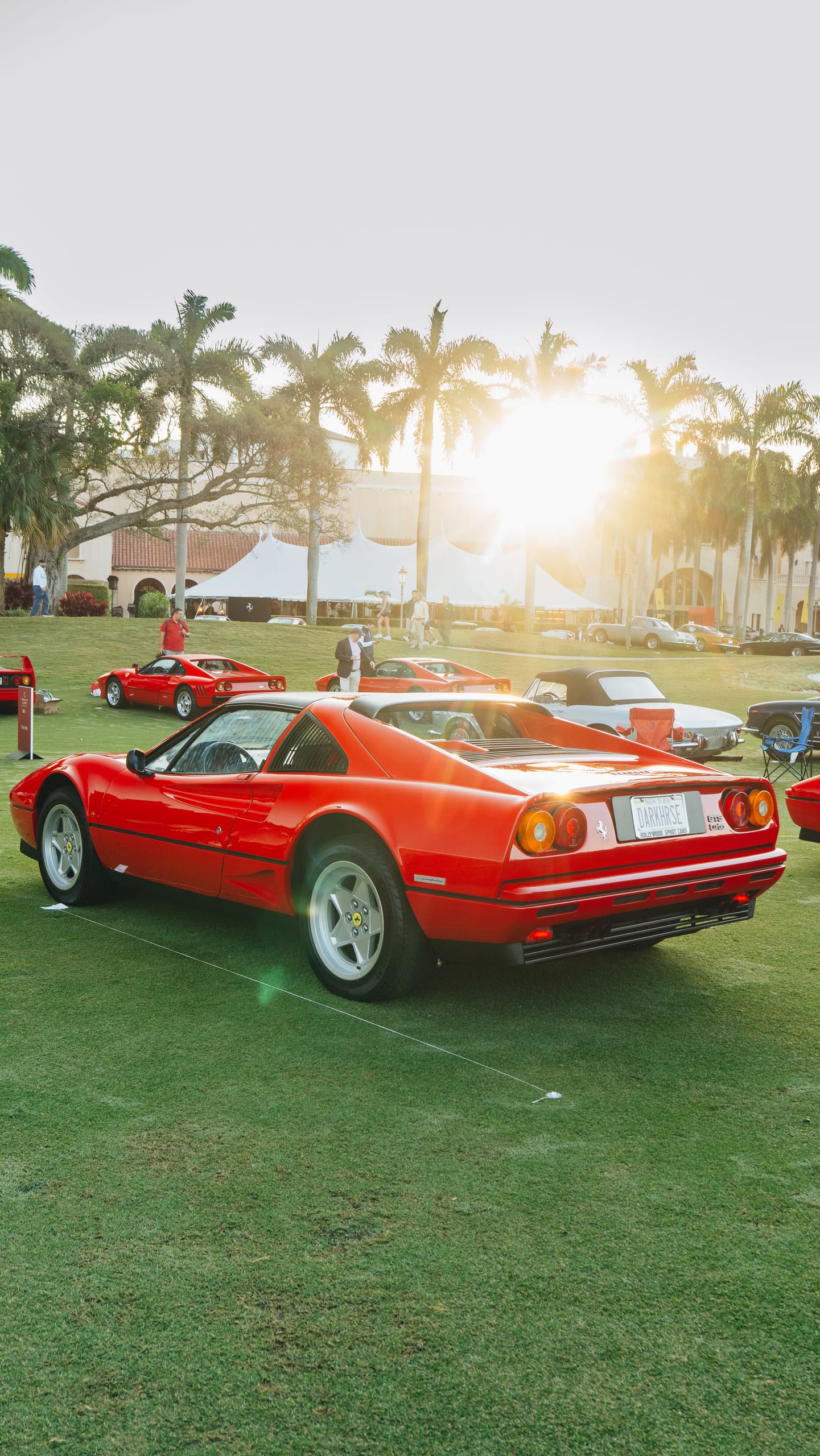 Red Ferrari 328 GTS on the concours lawn with hospitality tents and palm trees in the background