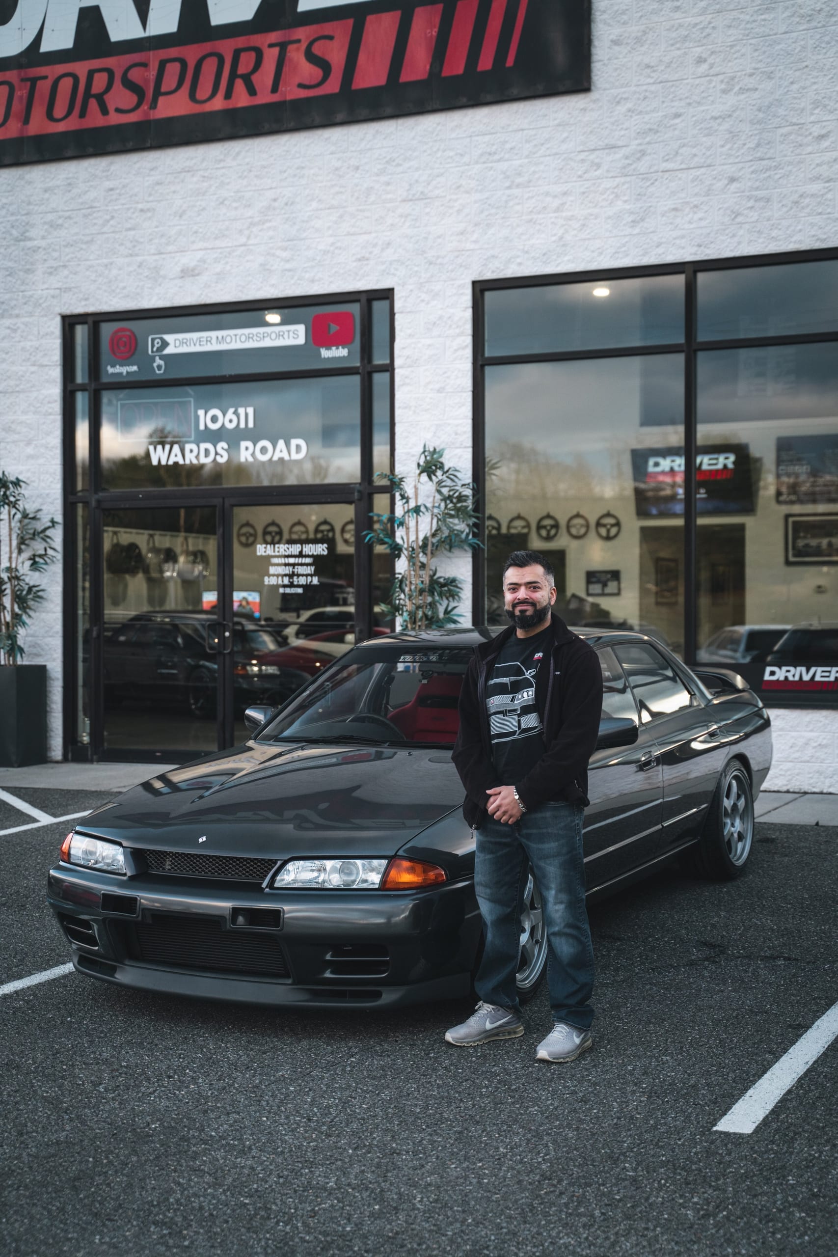 Owner standing with a Nissan Skyline R32 in front of the Driver Motorsports showroom