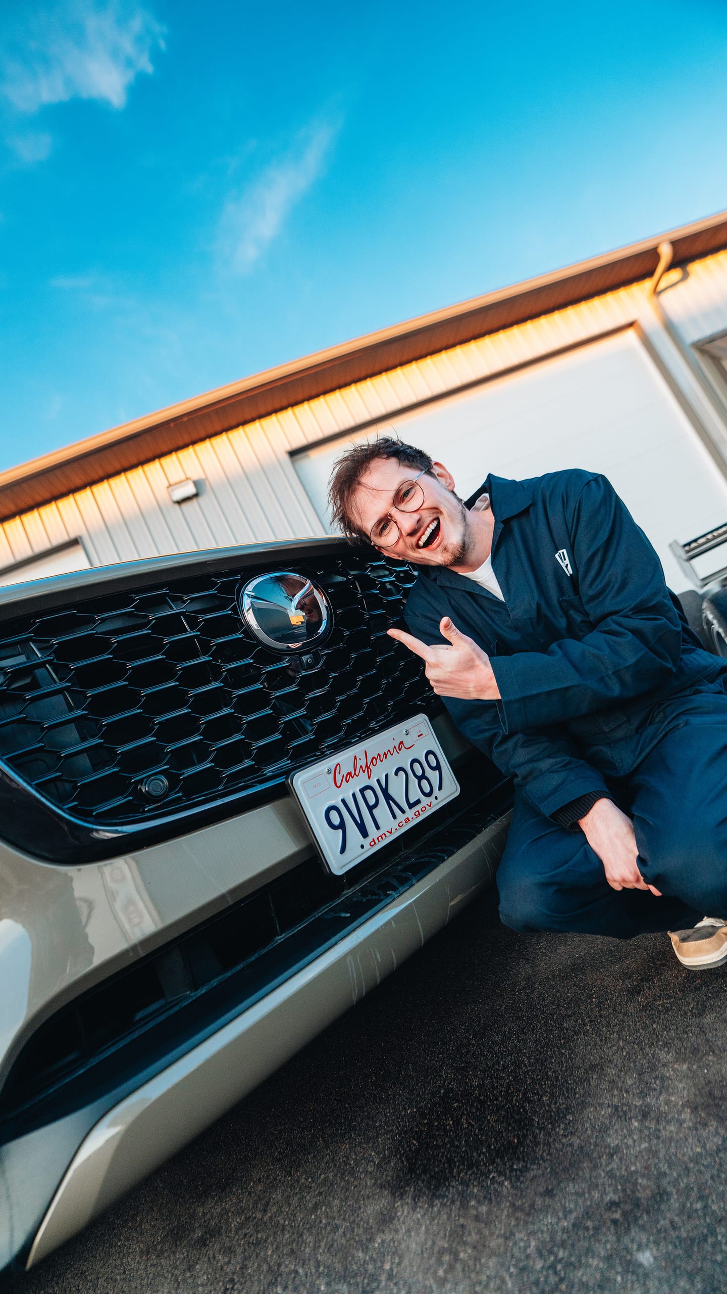 AlexMartini crouching next to the front grille of a Mazda CX-70 at a racing event