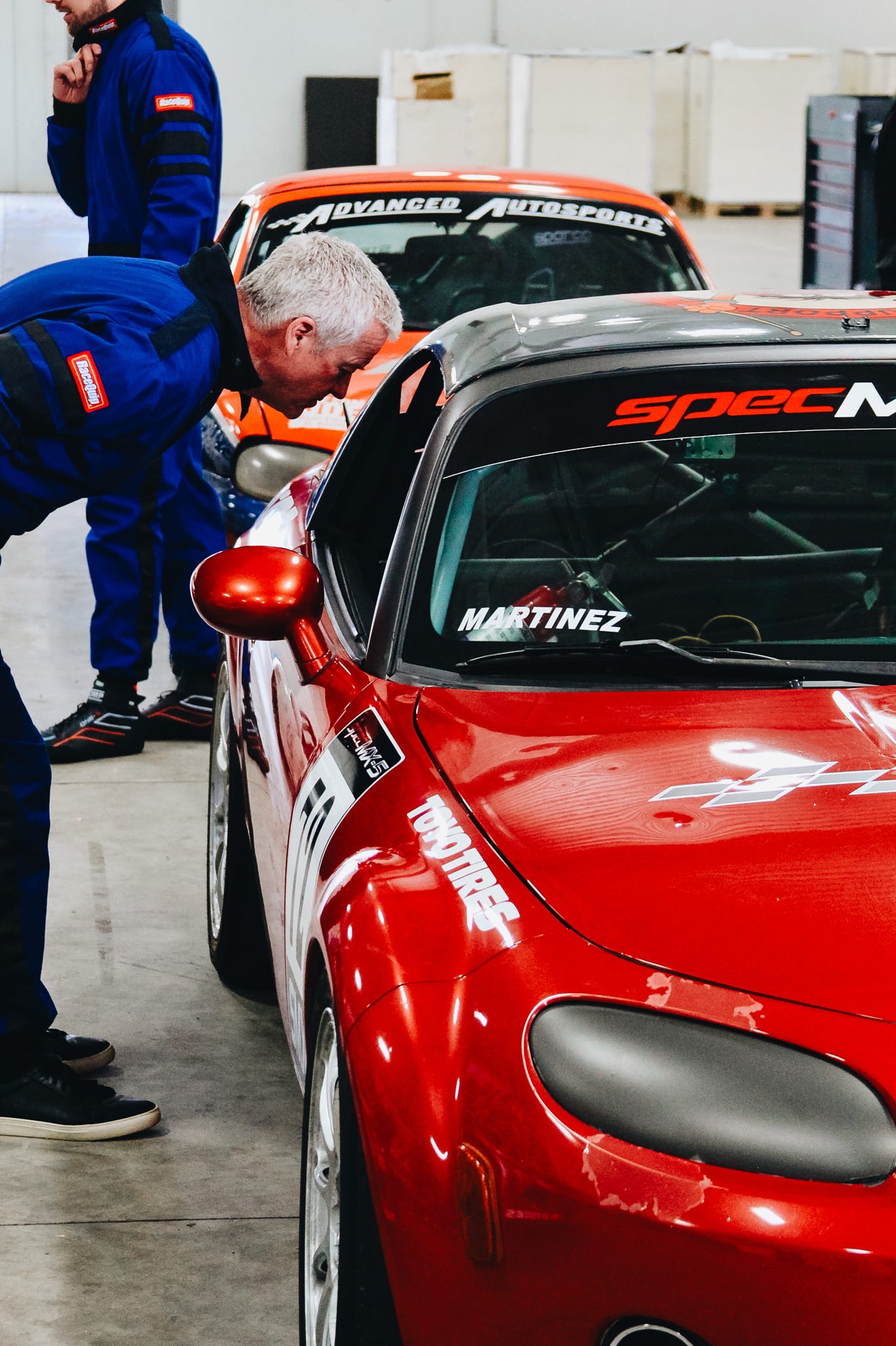 Racing instructor inspecting a red Spec MX-5 in the garage at a Mazda racing school