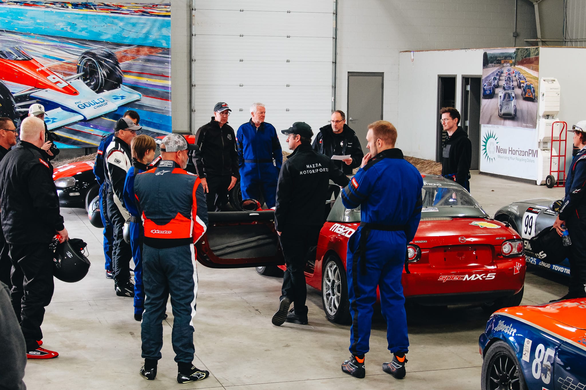 Drivers gathered around Spec MX-5 race cars during a Mazda Motorsports racing school briefing