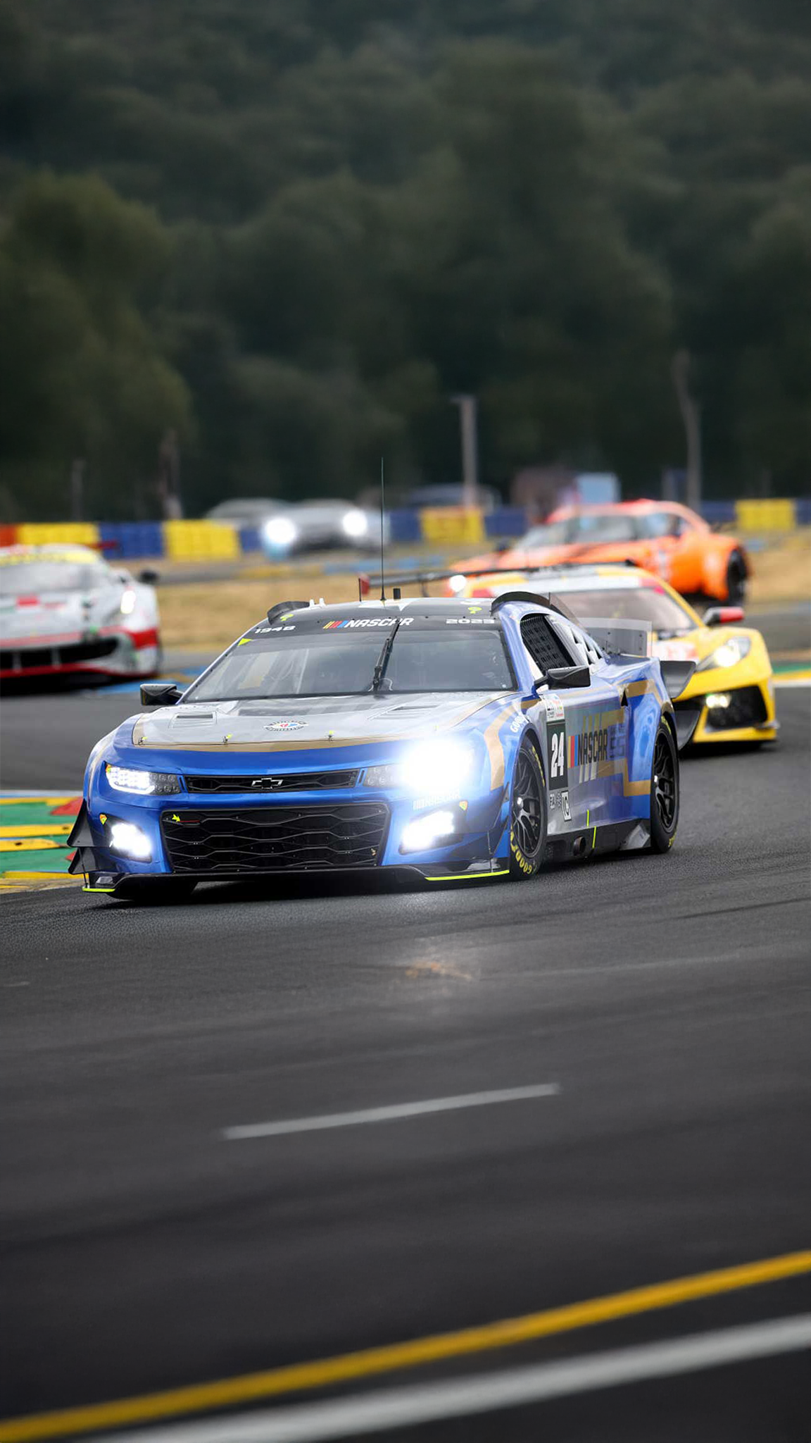 NASCAR Garage 56 car racing on track with headlights on amid a pack of competitors