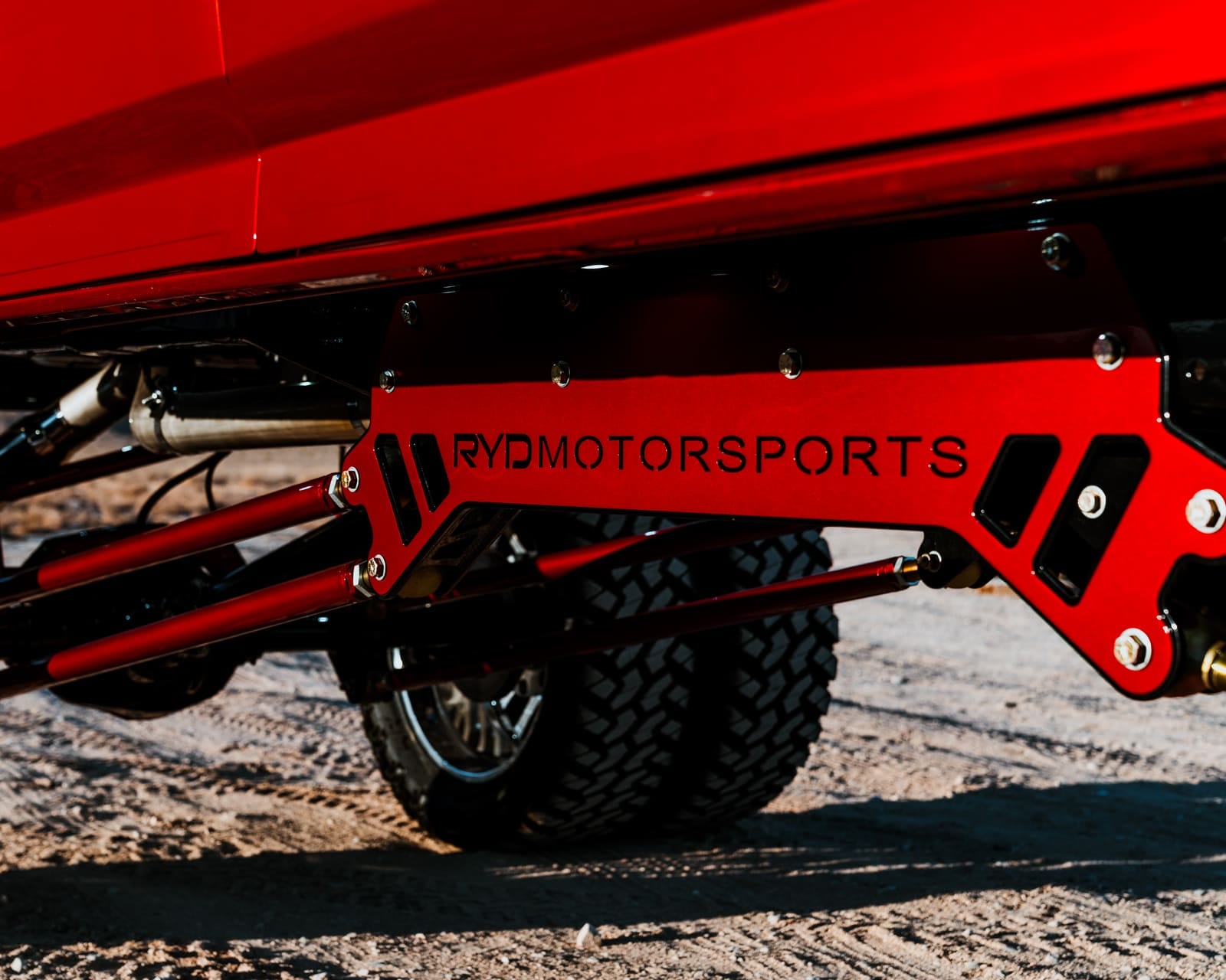 Closeup of a red fabricated RYD Motorsports traction bar bracket with the logo cut into the plate