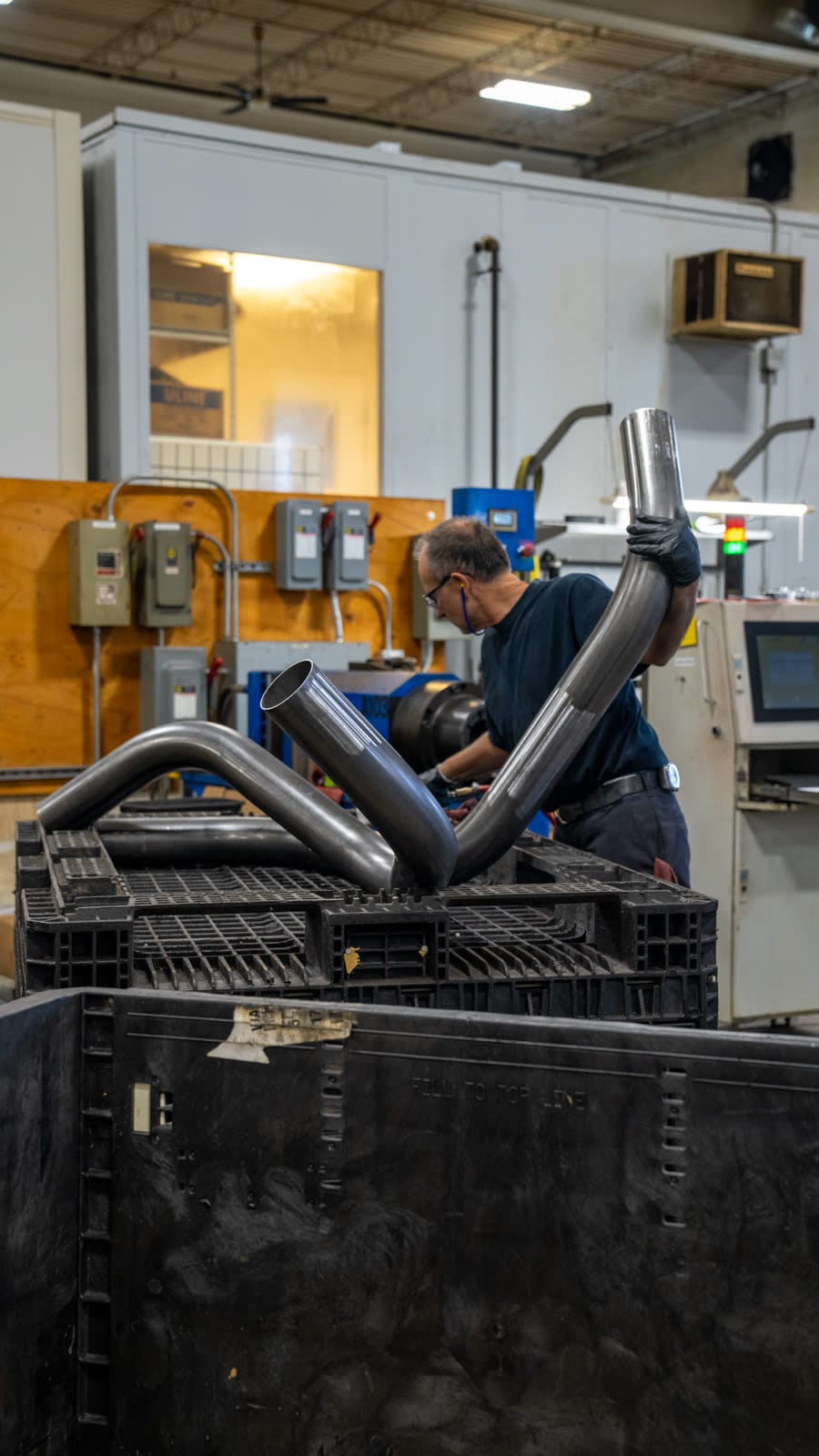 Sharpe Products technician operating a CNC tube bender with finished bends in the foreground