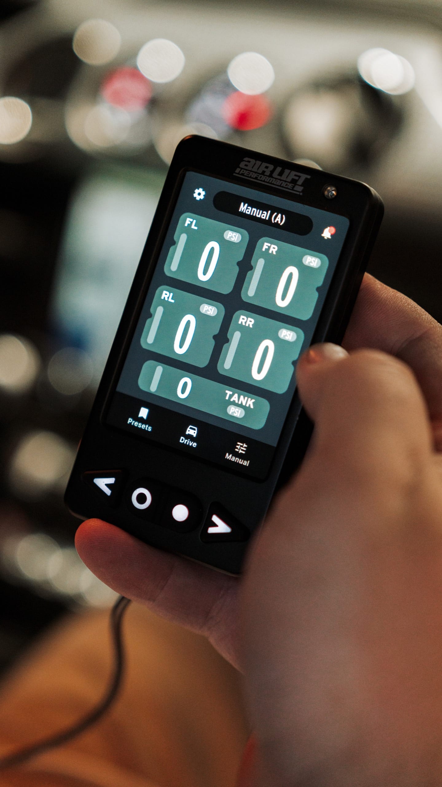 Hand holding the Air Lift Performance 3P controller showing live air pressure at each corner