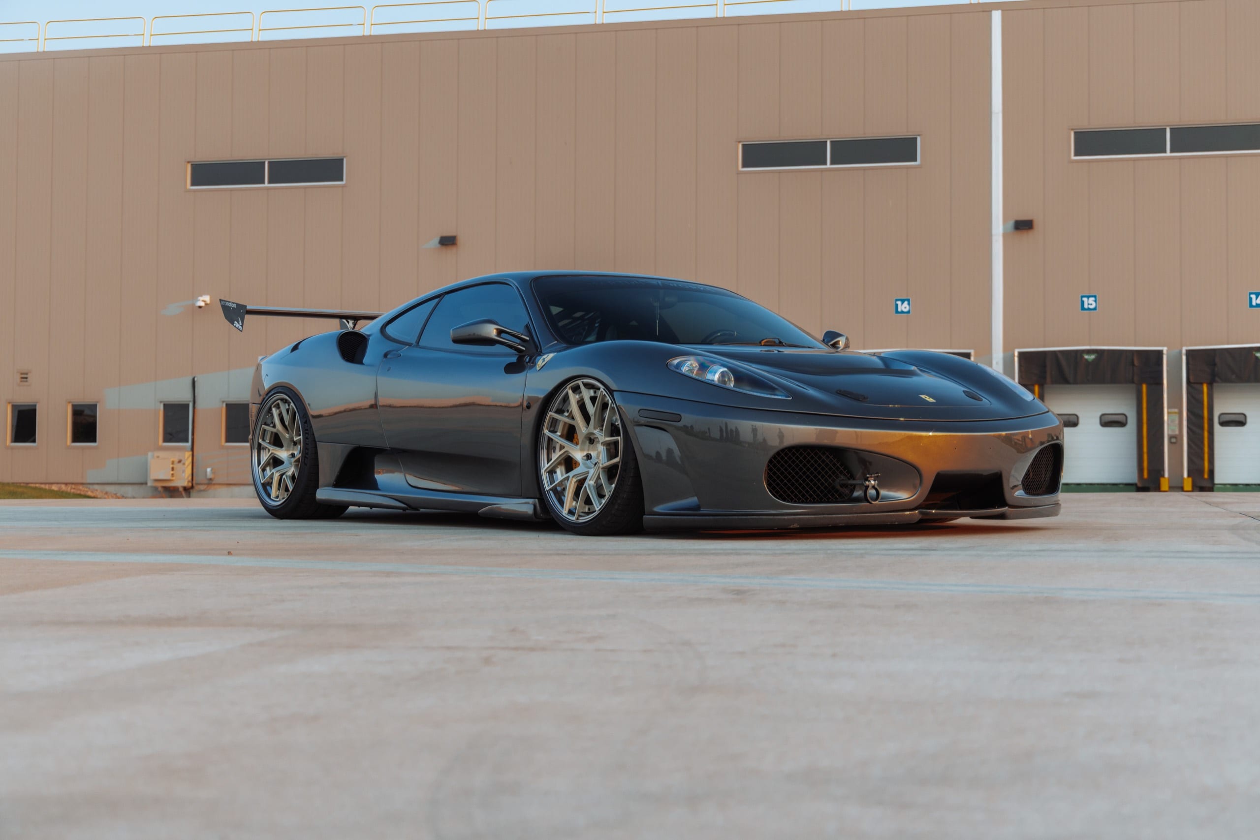 Air-suspended Ferrari F430 sitting low on polished wheels outside a warehouse