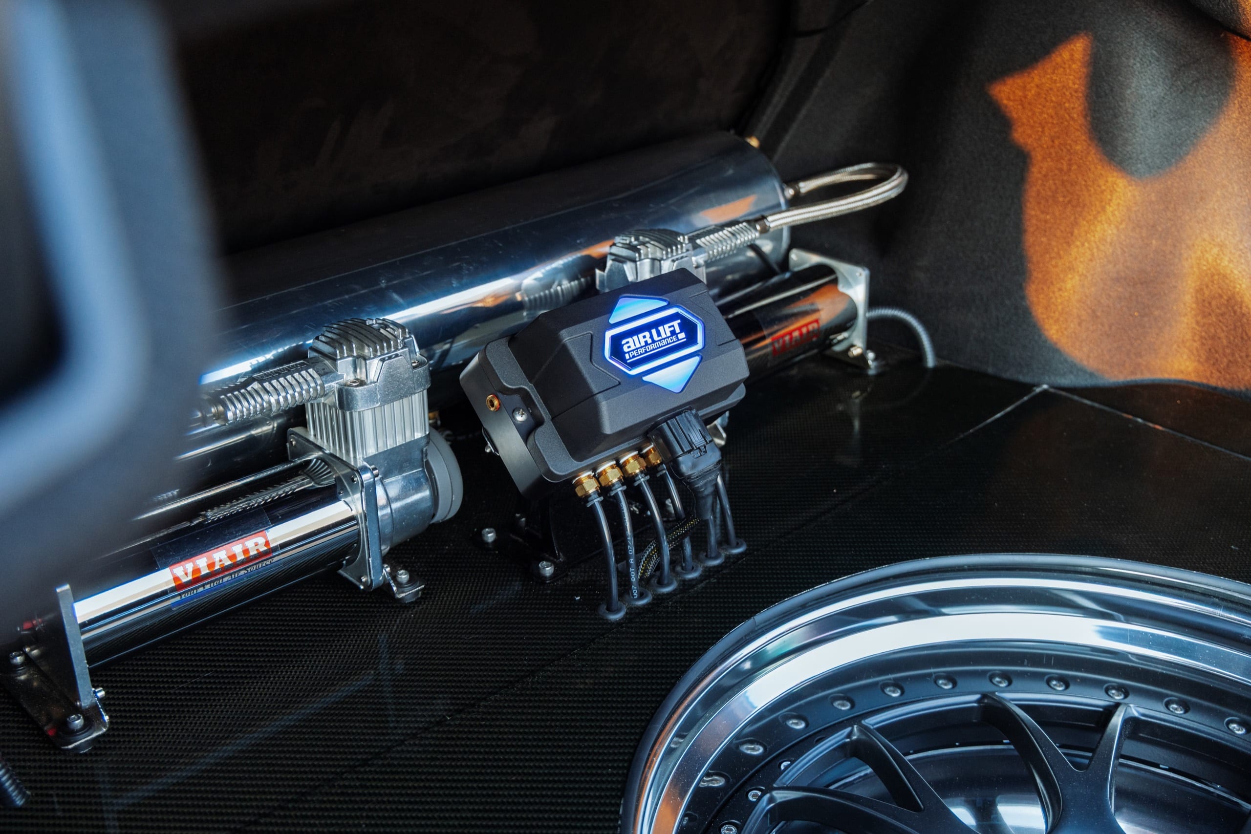 Trunk-mounted Air Lift Performance air management: compressors, tank, and manifold beside a polished wheel