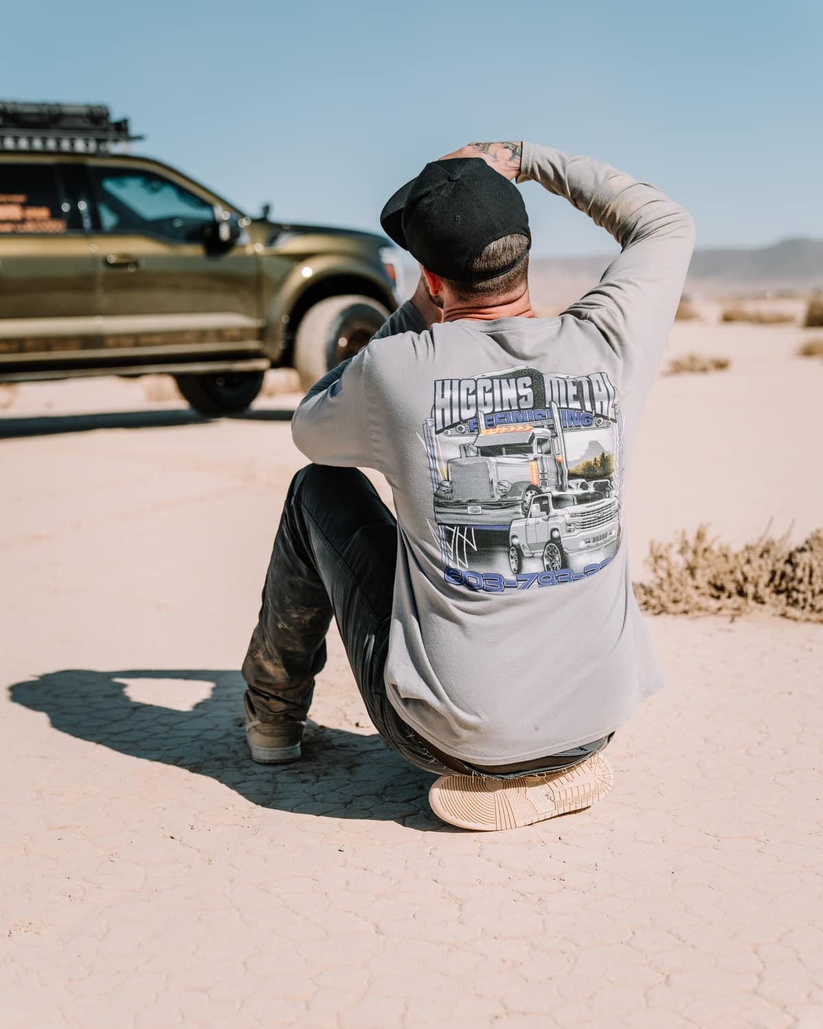 A builder in branded apparel beside an overland truck in the desert