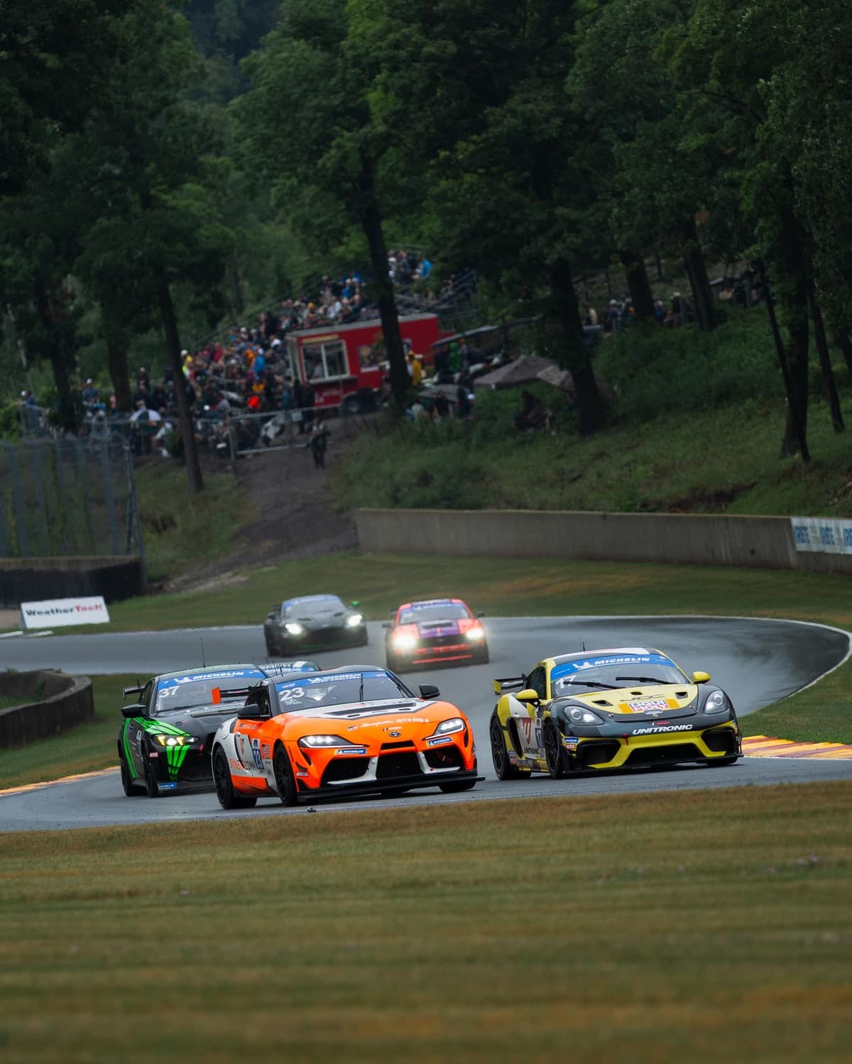 A pack of GT4 race cars leading the field past the grandstands