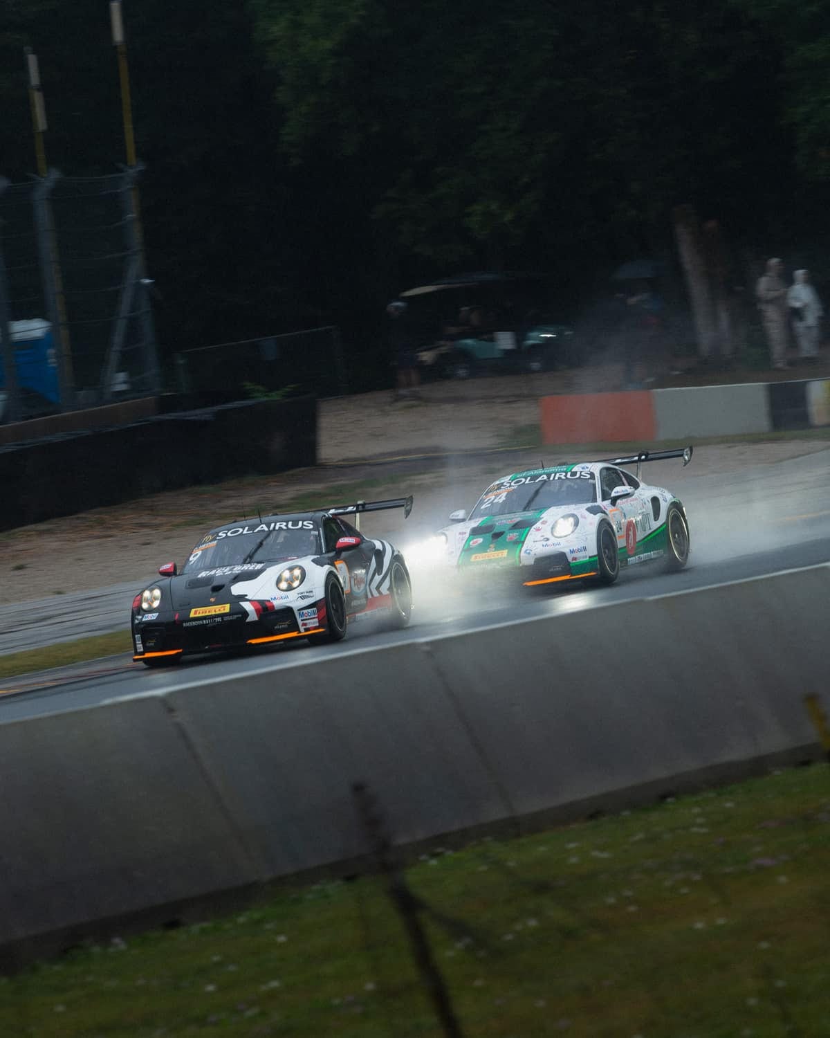 Two Porsche GT3 cars racing wheel to wheel in the rain