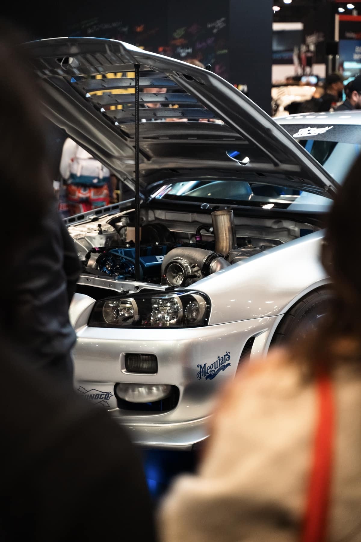 A Nissan Skyline R34 GT-R with its hood up on the trade show floor
