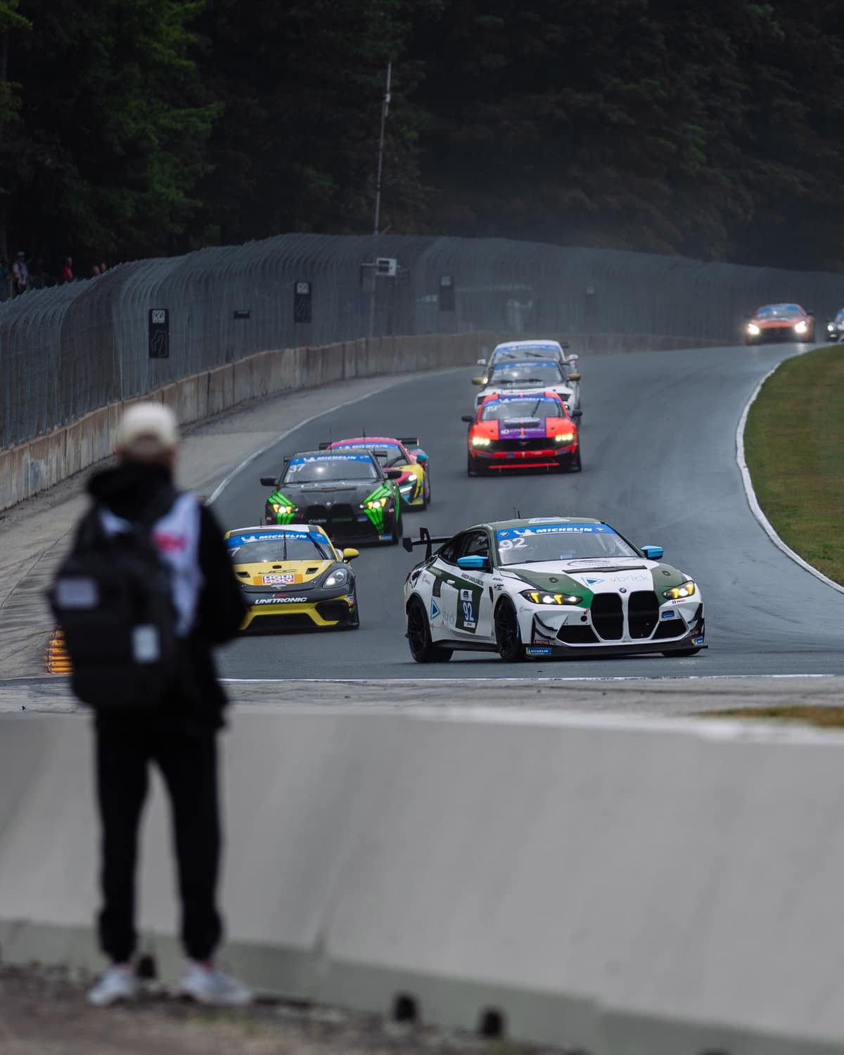 A spectator watching the field of race cars come through a corner trackside