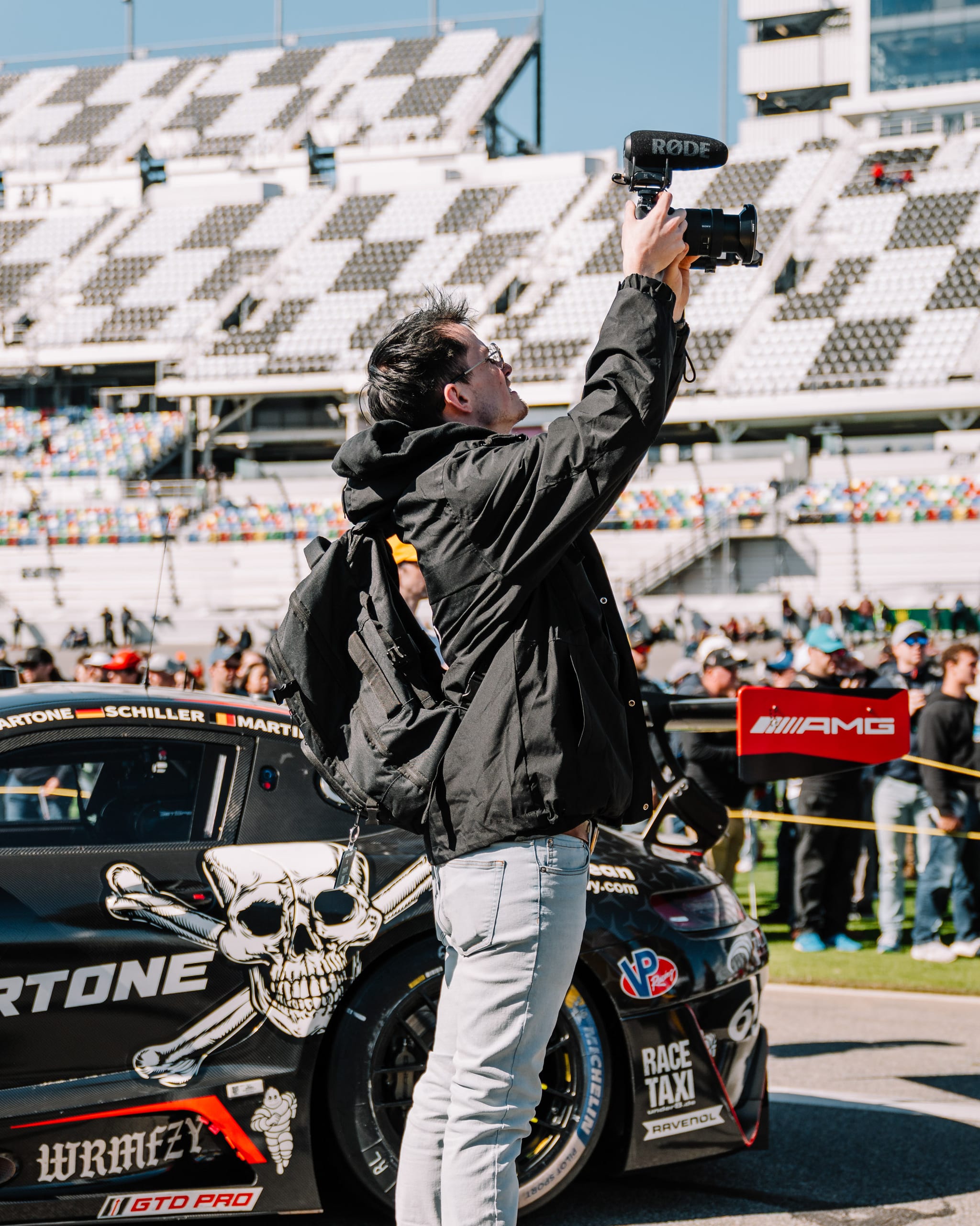 MetaMartini creator filming social content with a camera and microphone in front of an AMG GT race car at the Rolex 24 at Daytona